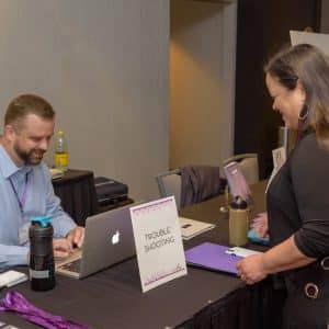 Friendly guest interaction at event registration table for troubleshooting assistance