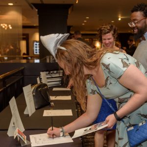 Woman wearing shark-themed dress and shark-fin headband placing her bid for a silent auction prize