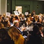 People at Center for Women's Leadership luncheon sitting around tables with some bid paddles raised in the air