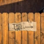 Wooden sign reading THIS WAY affixed onto wooden fence